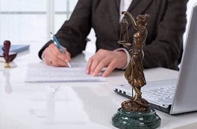 Statue of the woman holding a balance scale, In background businessman writing on a paper with a laptop placed on a table