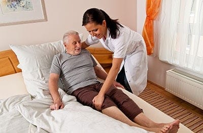 Female nurse helping an elderly man to get him in the bed
