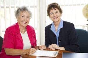 Elderly woman signing a power of attorney documents with a representative in office